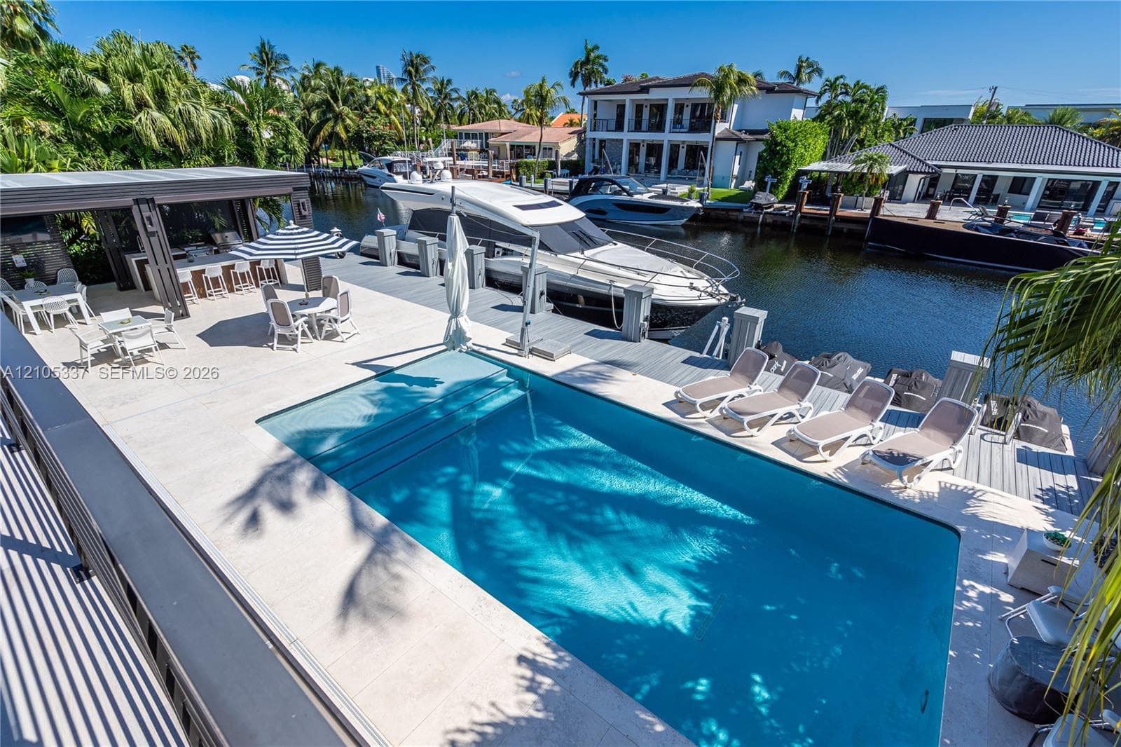 Waterfront terrace featuring a swimming pool, covered outdoor kitchen with bar seating, and deep-water dockage