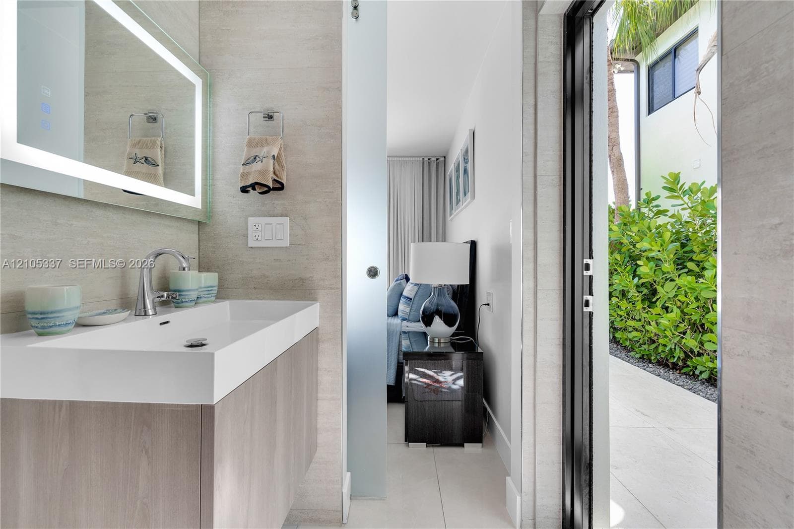 Modern floating vanity with a rectangular integrated sink, LED-backlit mirror, frosted glass sliding door, and stone-finish wall tile