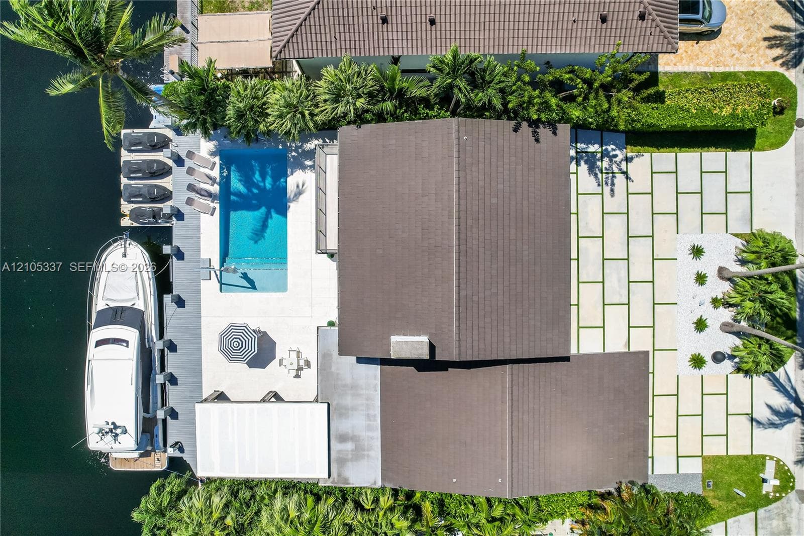 Waterfront property featuring a private boat dock, rectangular in-ground swimming pool, stone-paver hardscaping, and professional landscaping