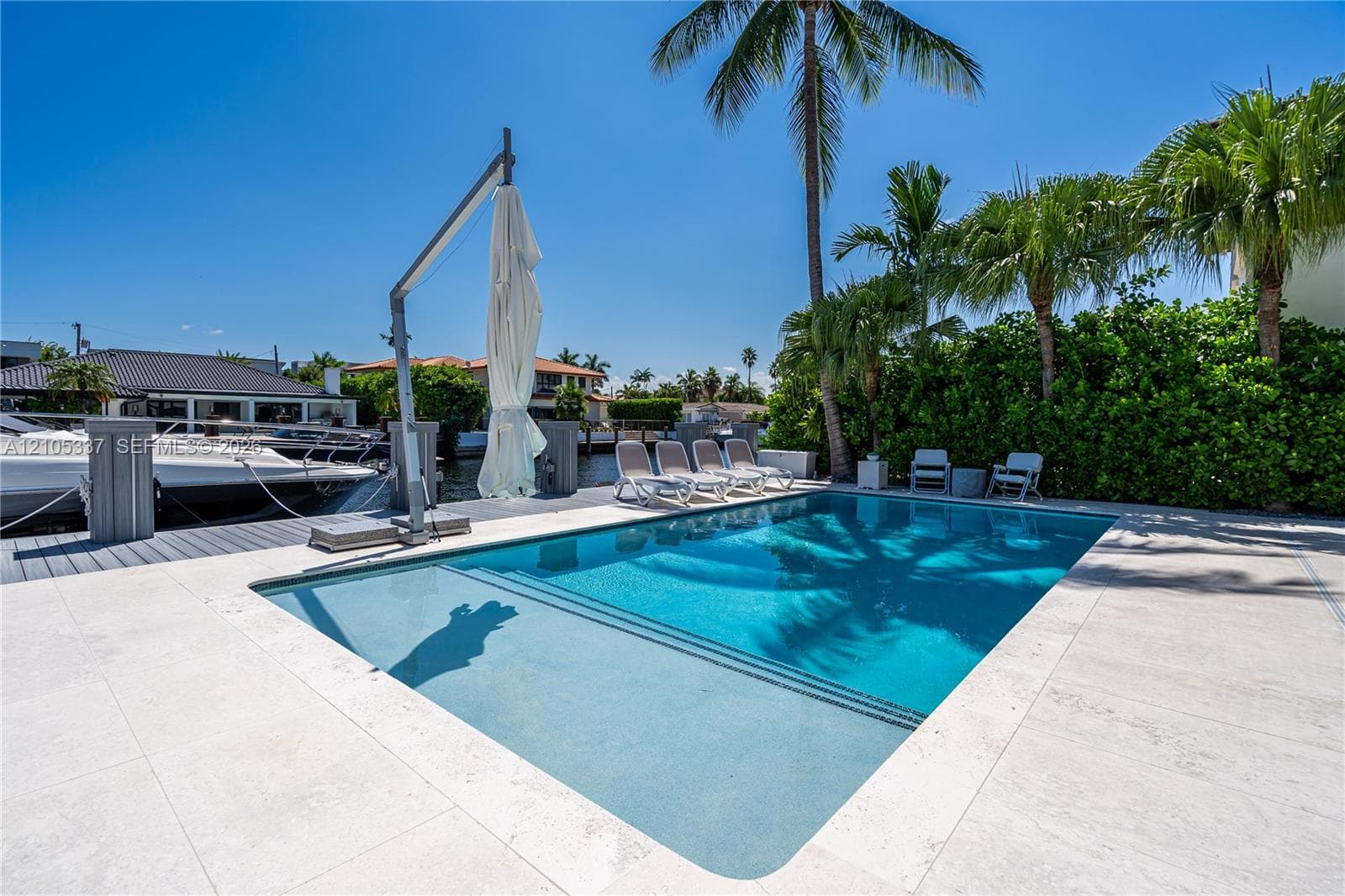 In-ground swimming pool with stone paver decking, dock access, and mature palm trees