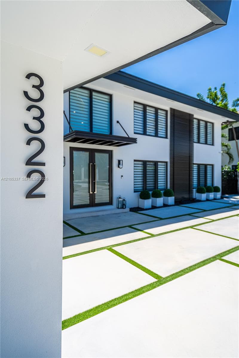 Modern two-story exterior featuring white stucco siding, a concrete paver driveway with turf accents, black-framed windows, and double glass-panel entry doors