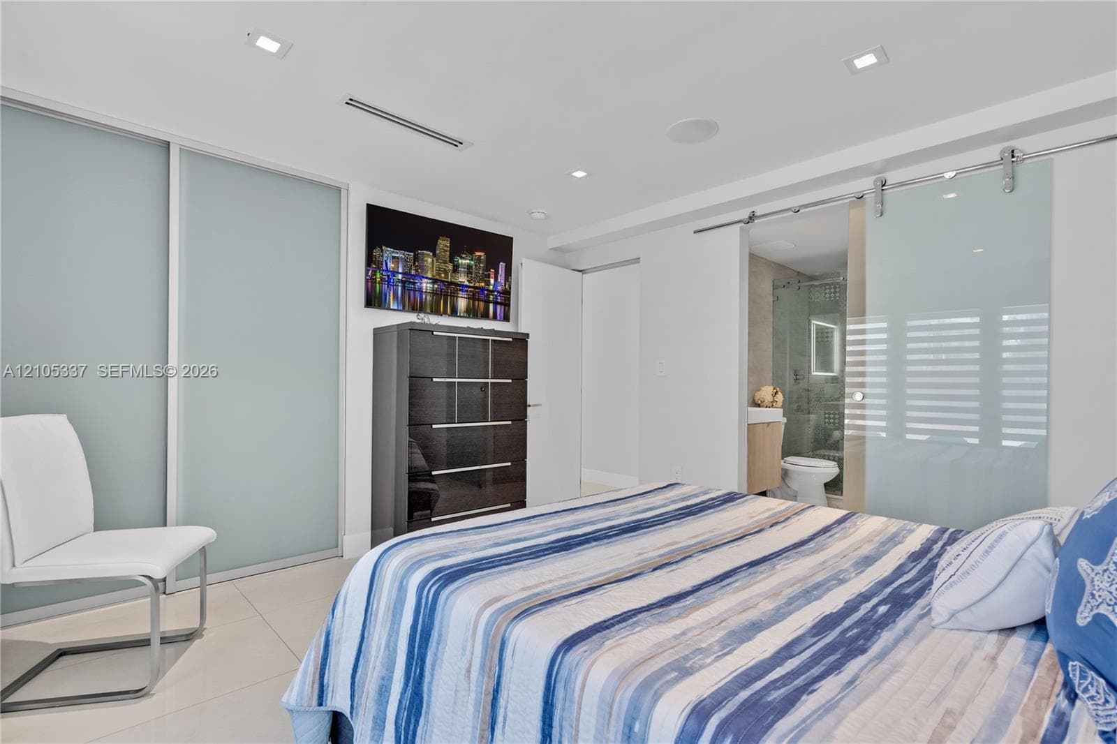 Frosted glass sliding closet doors, ceiling recessed lighting, polished tile flooring, and a frosted glass sliding barn door with stainless steel hardware