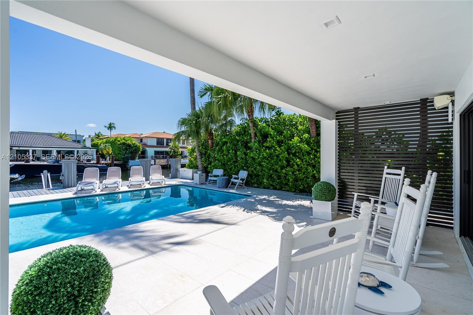 Covered patio with large-format tile flooring, horizontal slat privacy screening, recessed lighting, and a swimming pool set within a paved deck