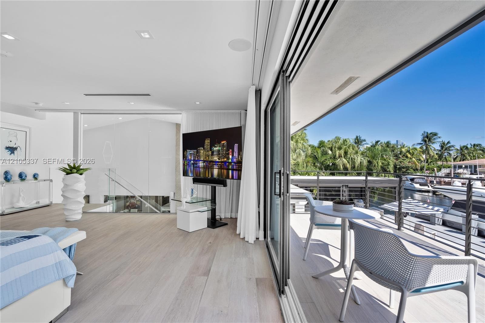 Floor-to-ceiling retractable glass doors, expansive covered balcony with cable railing, wood-finish flooring, and recessed ceiling lighting