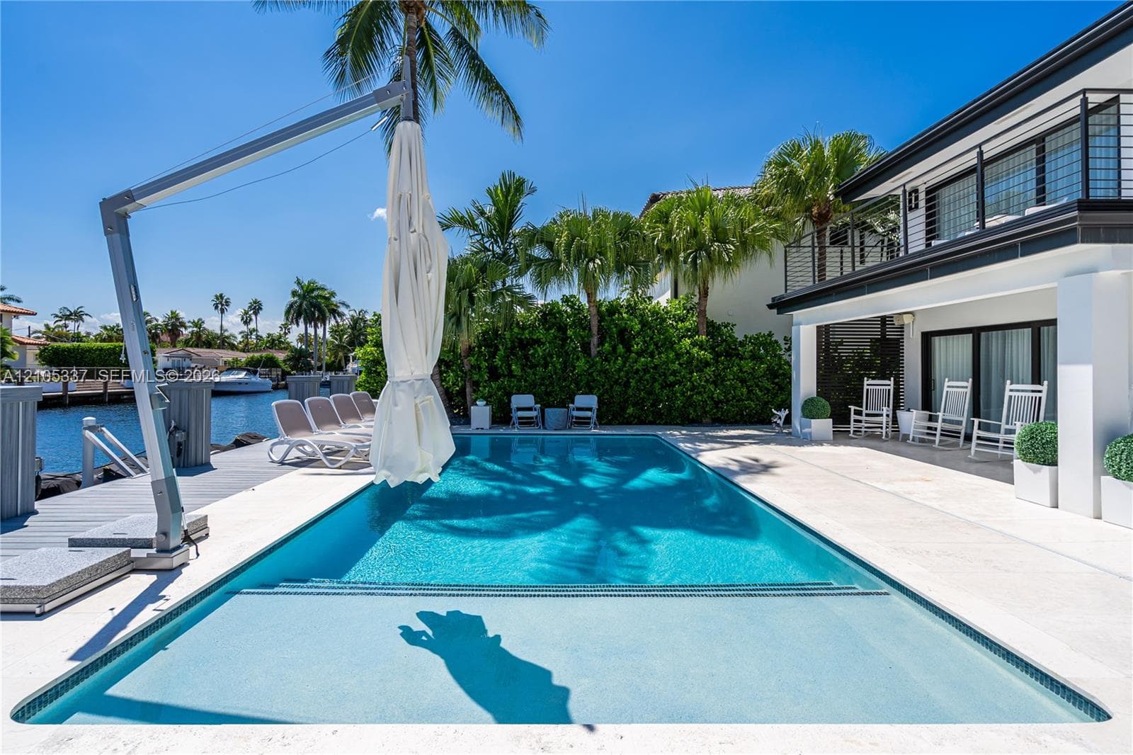 In-ground swimming pool with built-in tanning ledge, expansive stone pool deck, private waterfront dock, and second-story balcony with metal railing