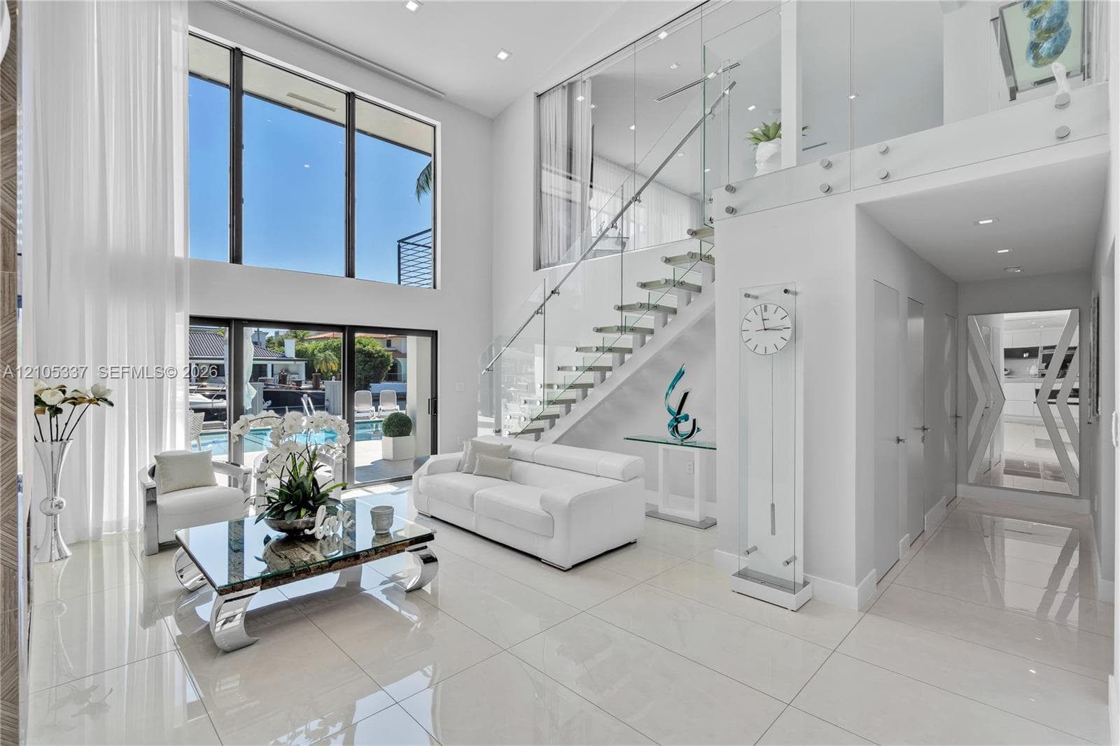 Double-height ceilings with floor-to-ceiling windows, open-riser staircase with glass balustrades, polished tile flooring, and recessed lighting