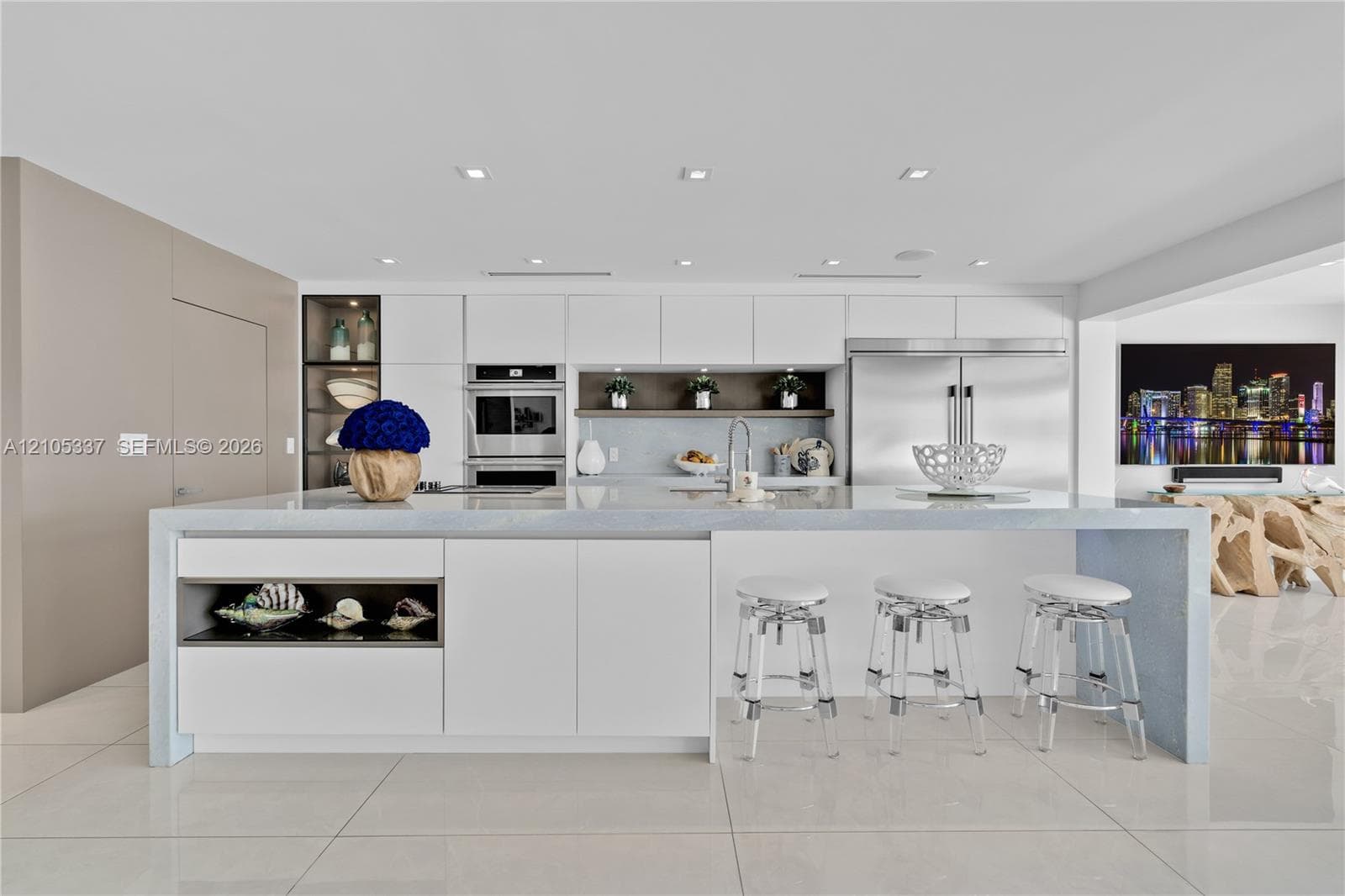 Modern kitchen featuring a waterfall-edge island, flat-panel cabinetry, stainless steel built-in appliances, recessed lighting, and large-format tile flooring