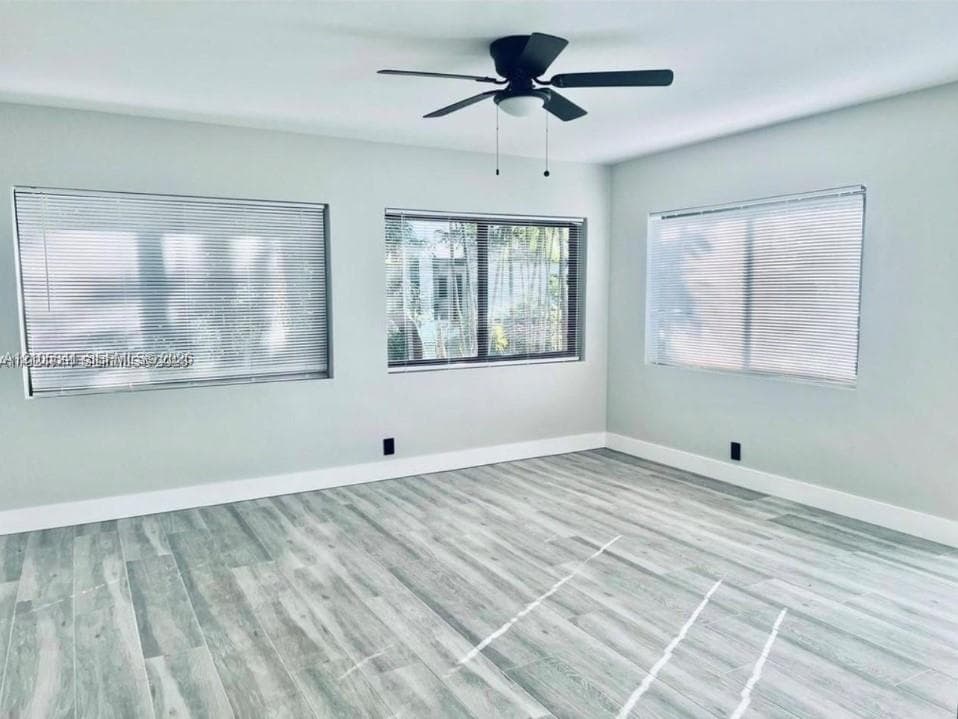 Interior space featuring wood-finish flooring, three large windows with integrated blinds, and a matte black ceiling fan with a centered light fixture