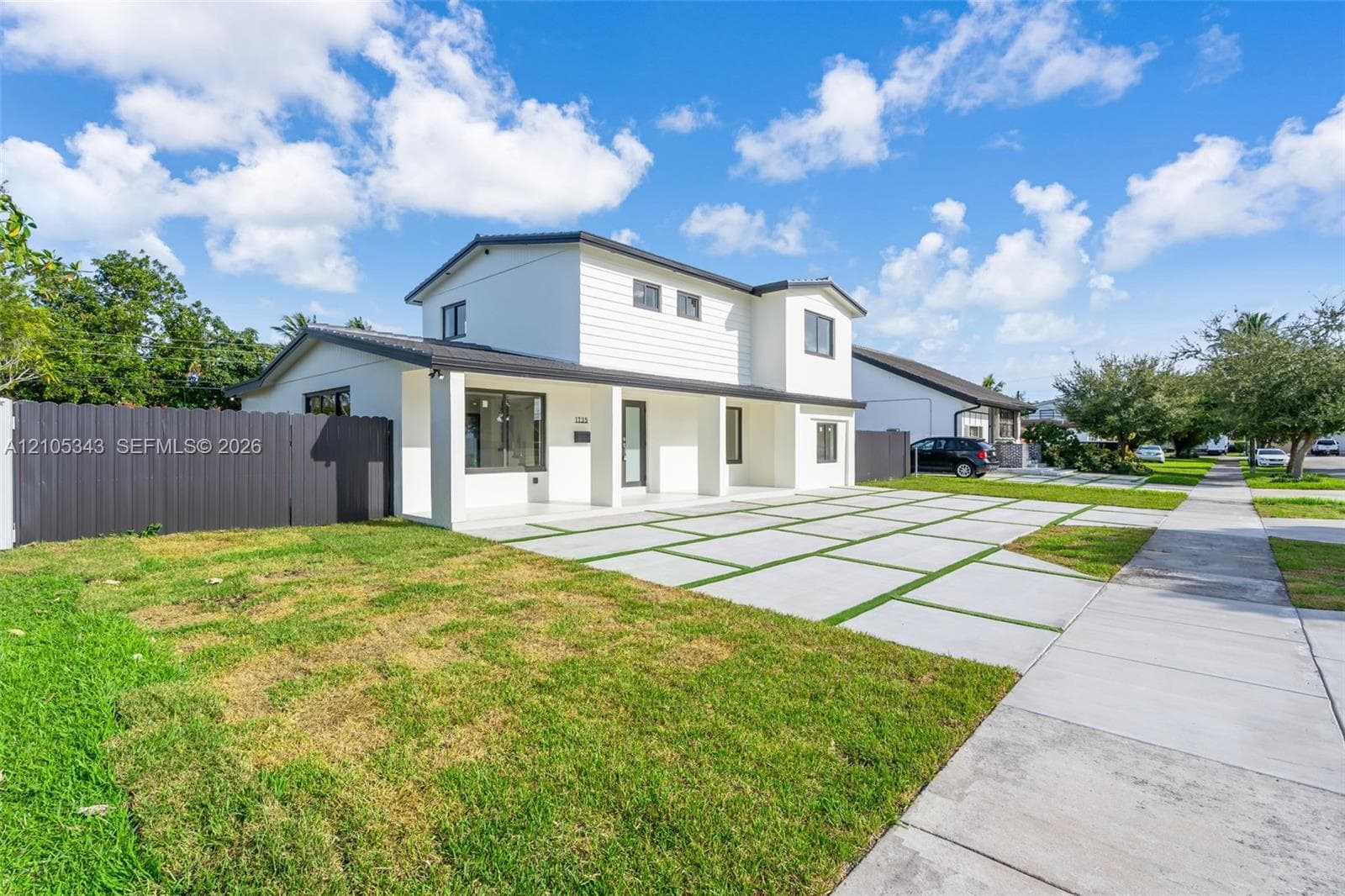 Two-story residence featuring a white horizontal siding exterior, a covered front entryway, and a concrete paver driveway with integrated turf grid accents, enclosed by a dark privacy fence