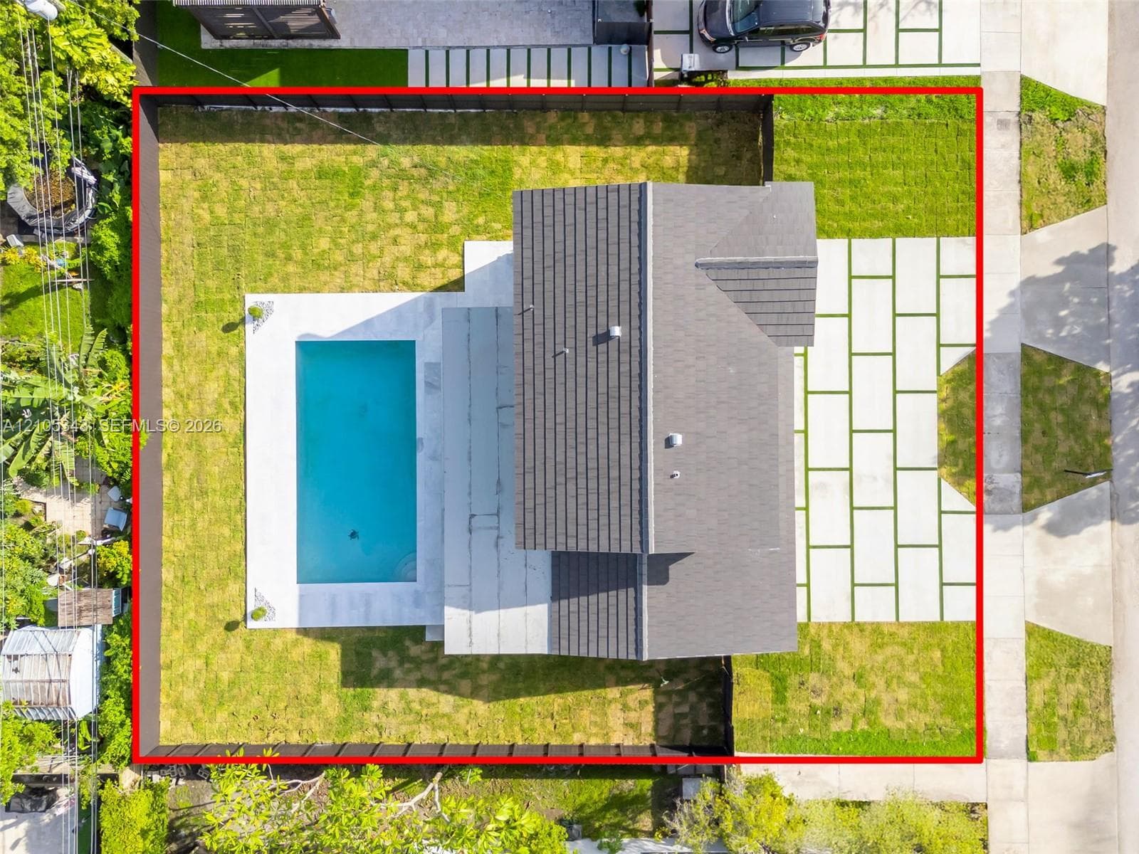 Aerial view of property featuring a swimming pool, concrete paver driveway with turf accents, fenced perimeter, and manicured lawn