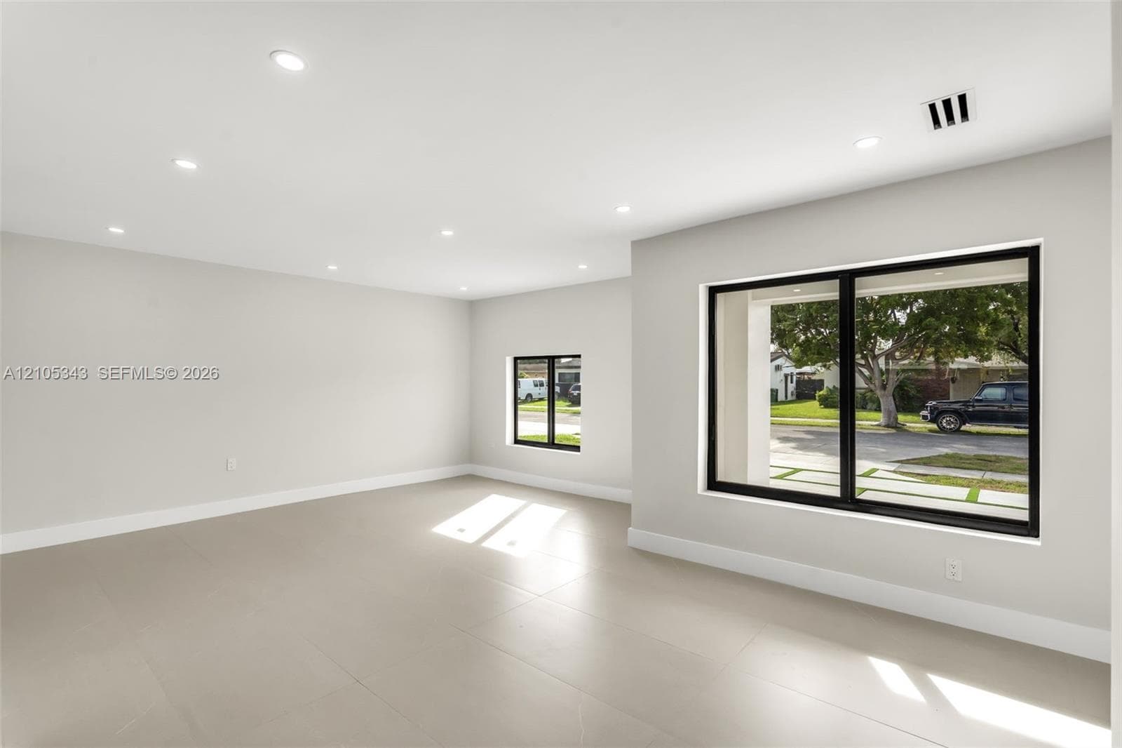Neutral-toned interior space featuring oversized rectangular tile flooring, recessed ceiling lighting, and black-framed windows
