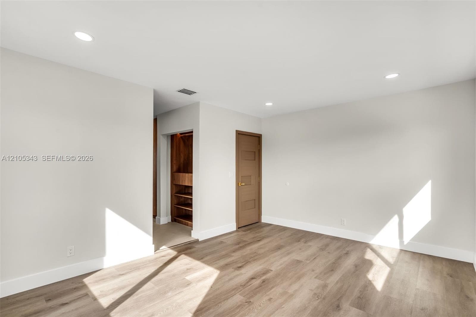 Neutral-toned walls, wood-finish flooring, recessed lighting, and a walk-in closet with built-in shelving
