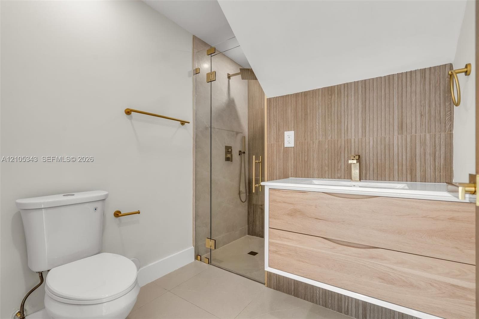 Floating wood-finish vanity with integrated sink, brass-tone hardware, vertical ribbed tile backsplash, and walk-in shower with glass enclosure