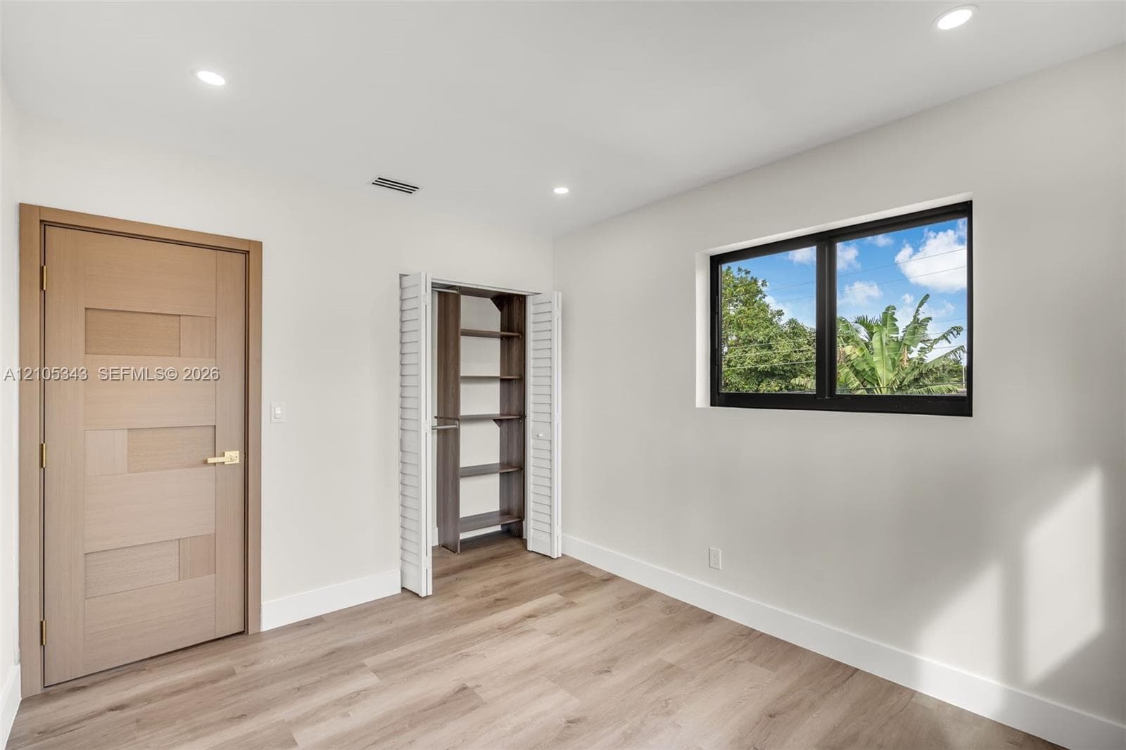 Wood-finish flooring, recessed lighting, interior door with a geometric paneled design, closet with built-in shelving, and a black-framed window