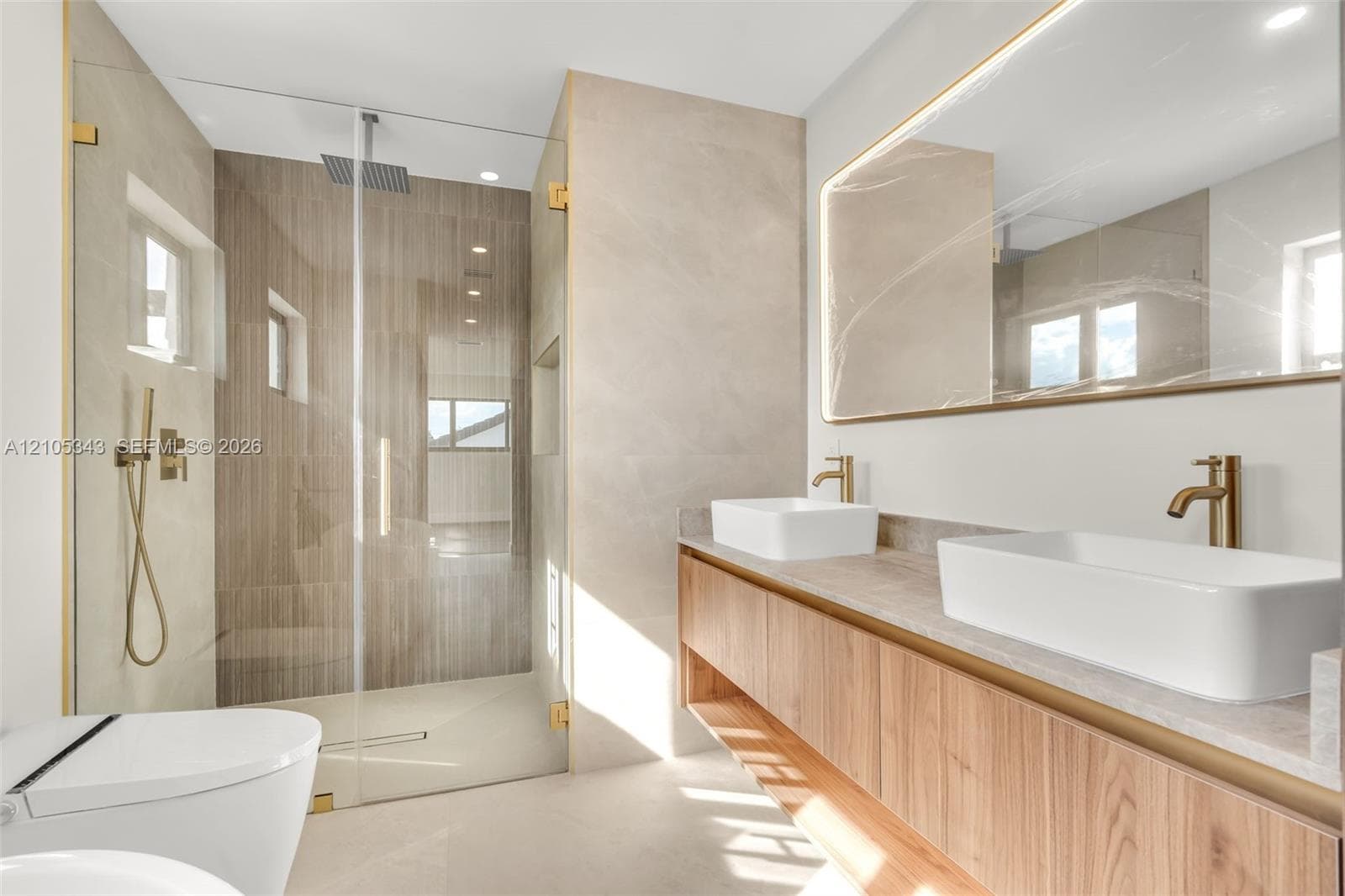 Floating wood-finish vanity with dual vessel sinks, quartz countertops, brass-toned hardware, and a frameless glass-enclosed shower with tiled walls