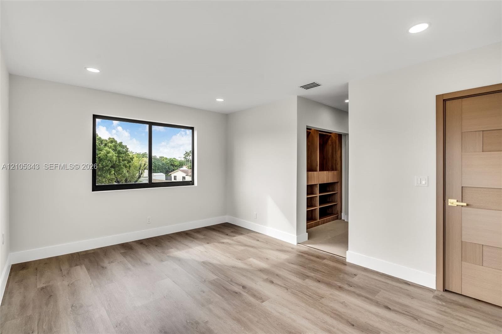Room featuring wood-finish flooring, recessed lighting, a horizontal sliding window with a dark frame, and a wood-finished door with metallic hardware, complemented by a built-in wooden closet system