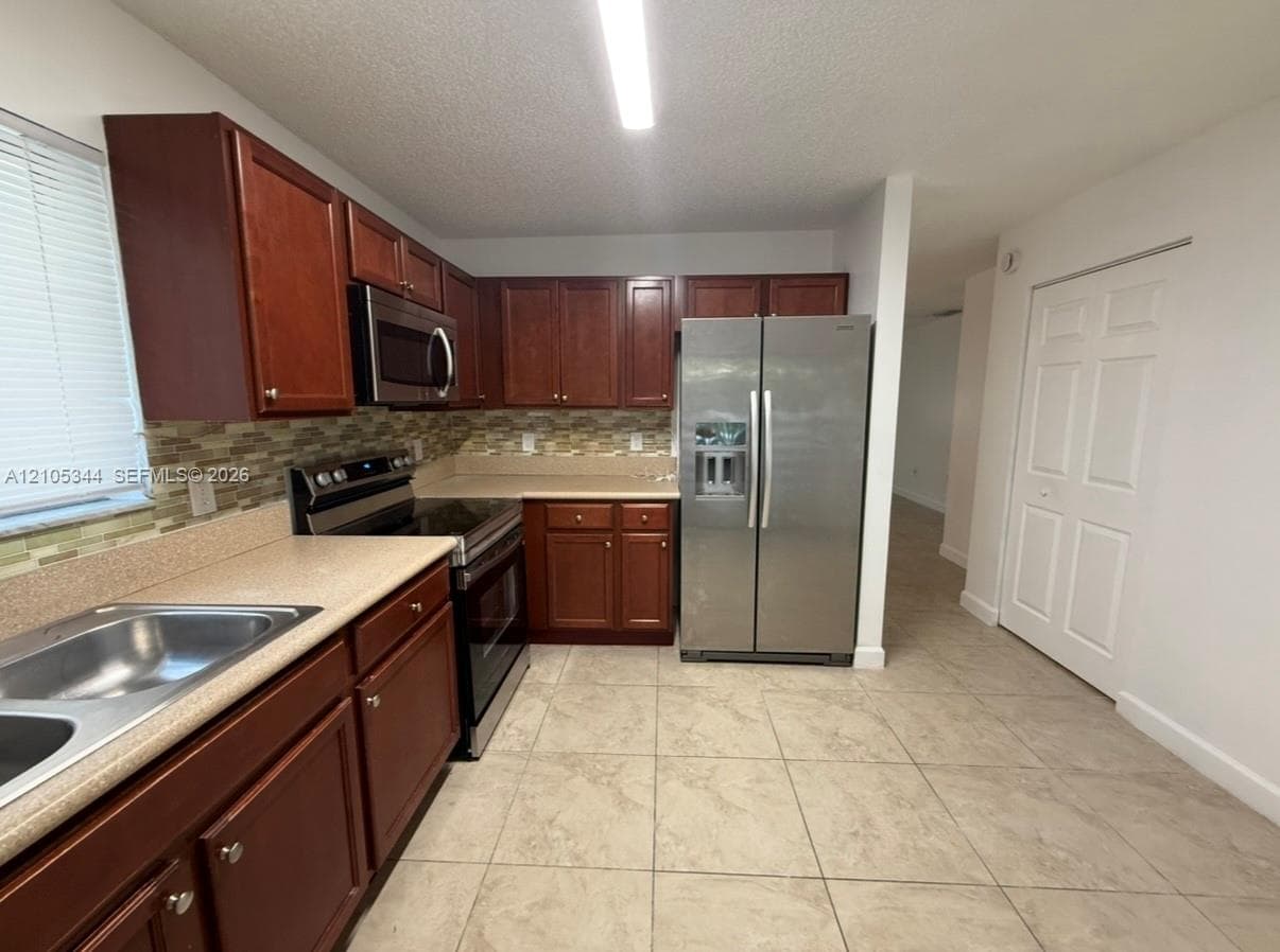Kitchen featuring wood-finish cabinetry, tile flooring, stainless steel appliances, and a mosaic tile backsplash
