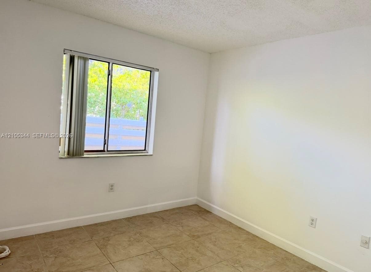 Neutral-toned tiled flooring, white painted walls, and a window with vertical blinds