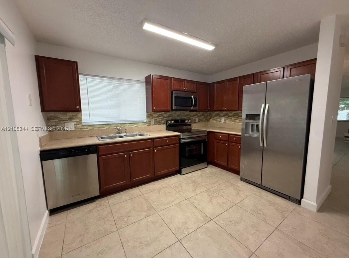 Kitchen featuring stainless steel appliances, wood-finish cabinetry, tile flooring, and a mosaic tile backsplash