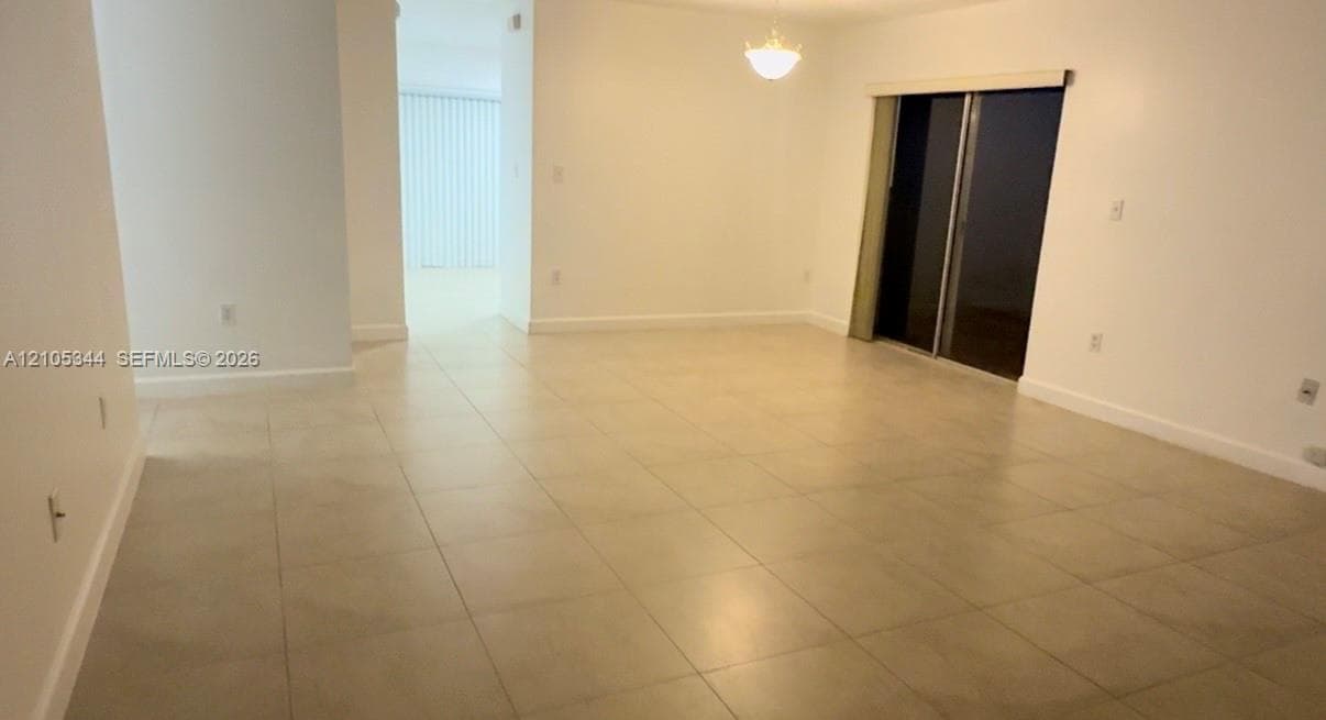 Light-colored tile flooring, overhead lighting, sliding glass door, white wall finishes, and a hallway