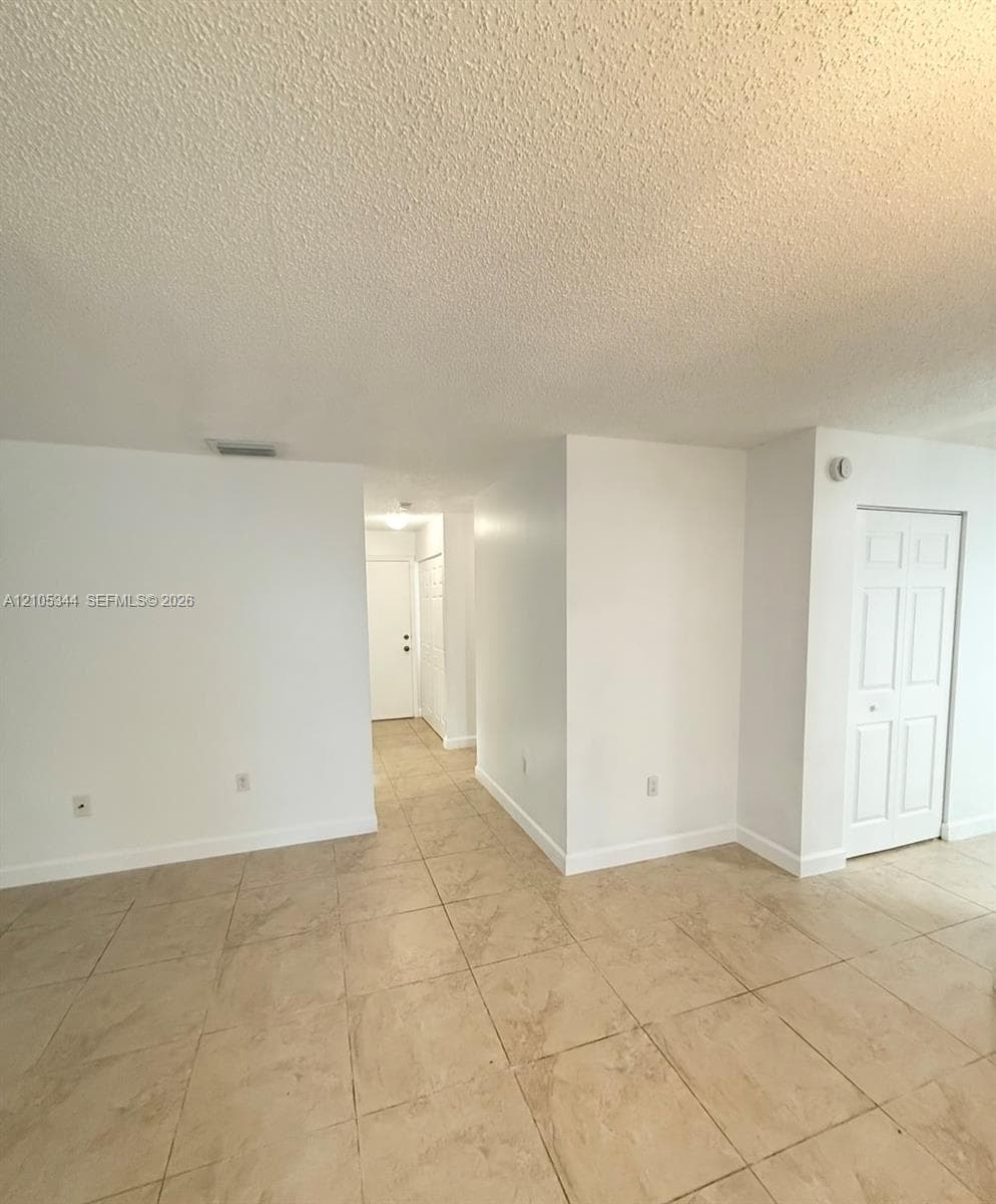 Neutral tone tiled flooring, white walls, and a textured ceiling