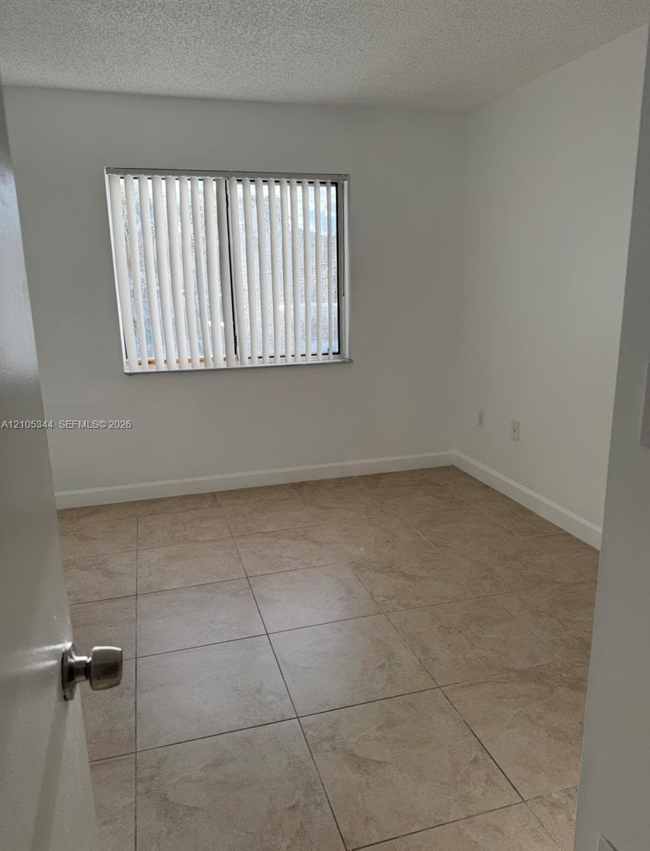 Neutral-toned tile flooring, window with vertical blinds, and white painted walls