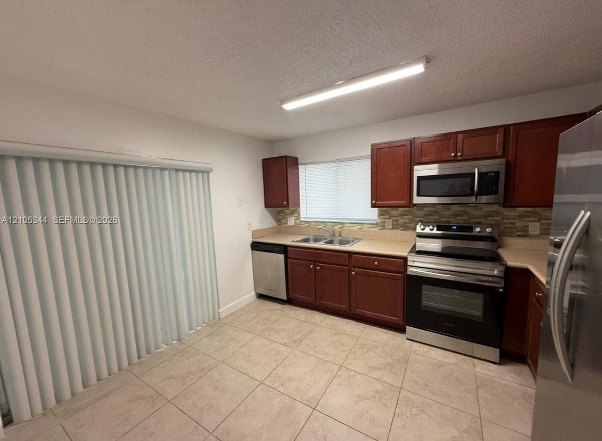 Kitchen featuring stainless steel appliances, wood cabinetry, light tile flooring, and a patterned backsplash