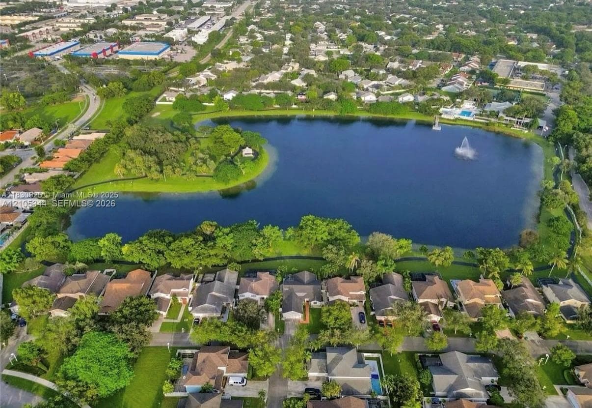 Expansive residential area featuring a large central lake with a fountain, surrounded by lush green landscaping and mature trees