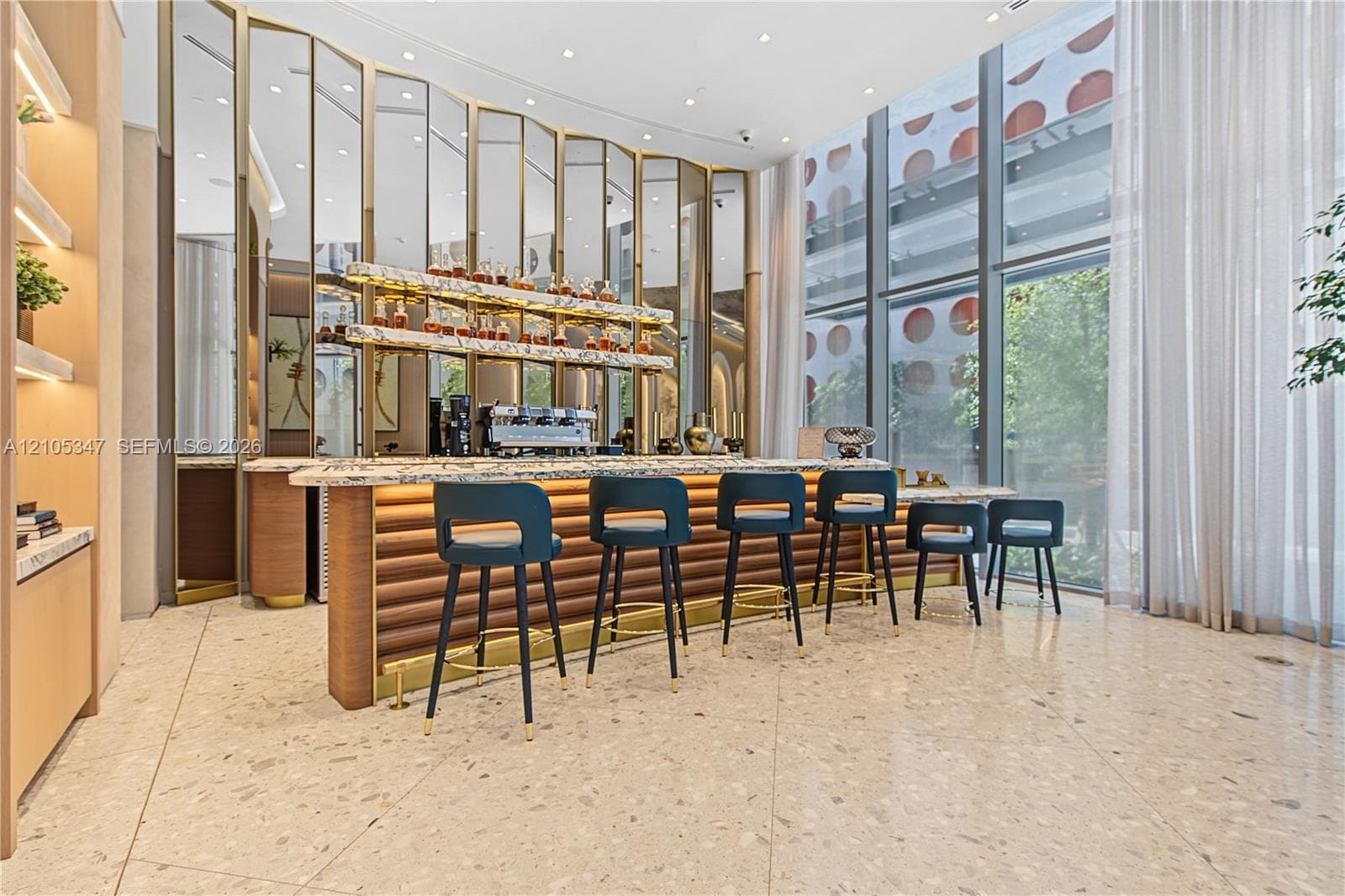 Custom bar featuring a stone countertop, tiered shelving with integrated lighting, a fluted wood-finish front panel, mirrored backsplash, and floor-to-ceiling windows
