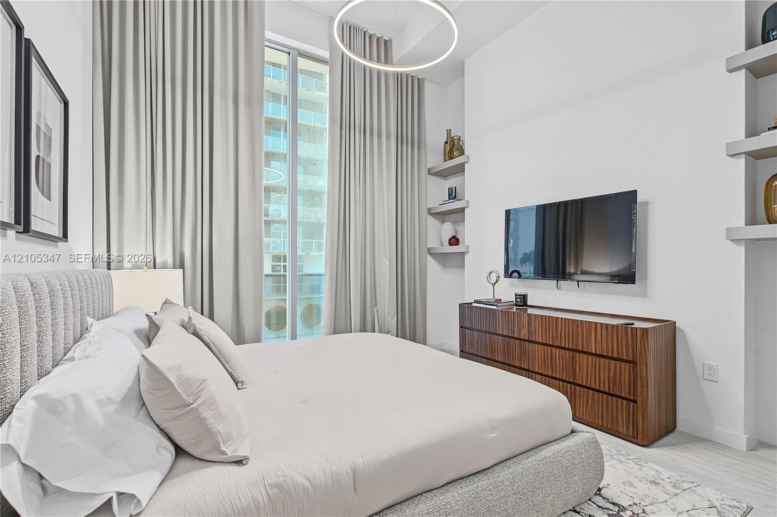 Floor-to-ceiling windows with full-length drapery, integrated wall shelving, wood-finish console, wall-mounted display, and an overhead circular light fixture