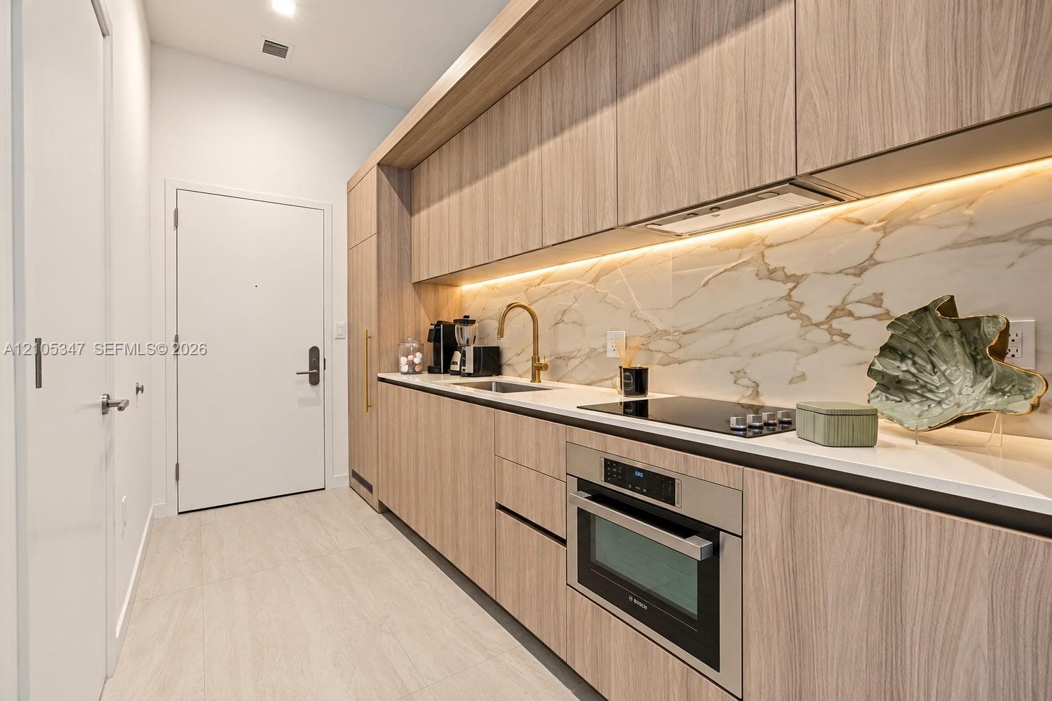Kitchenette featuring wood-finish cabinetry, integrated appliances, natural stone backsplash, undermount sink, and wood-finish flooring
