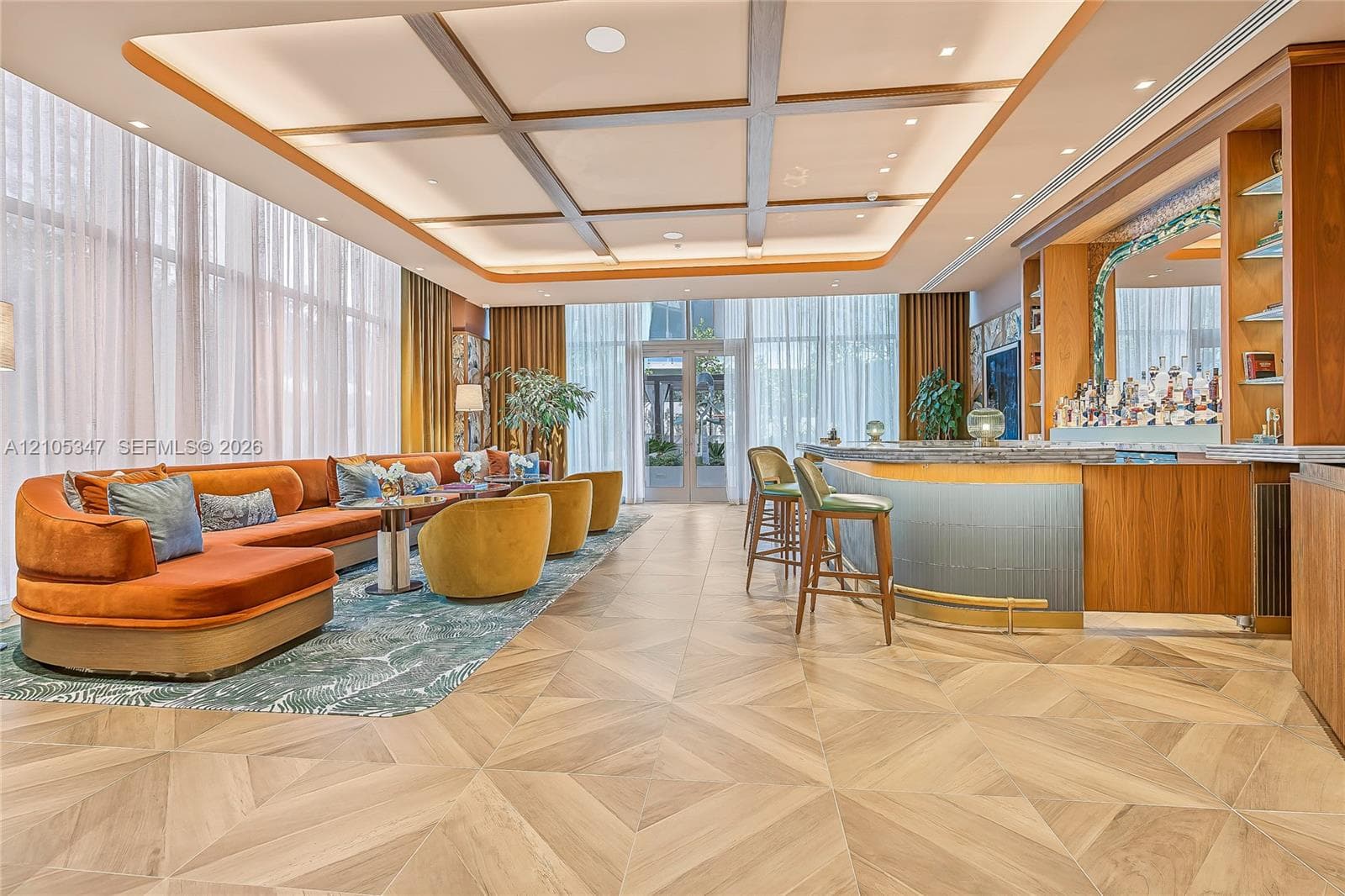 Coffered ceiling with recessed lighting, full-height windows, wood-finish geometric flooring, and custom built-in bar with stone-surfaced counter and brass foot rail