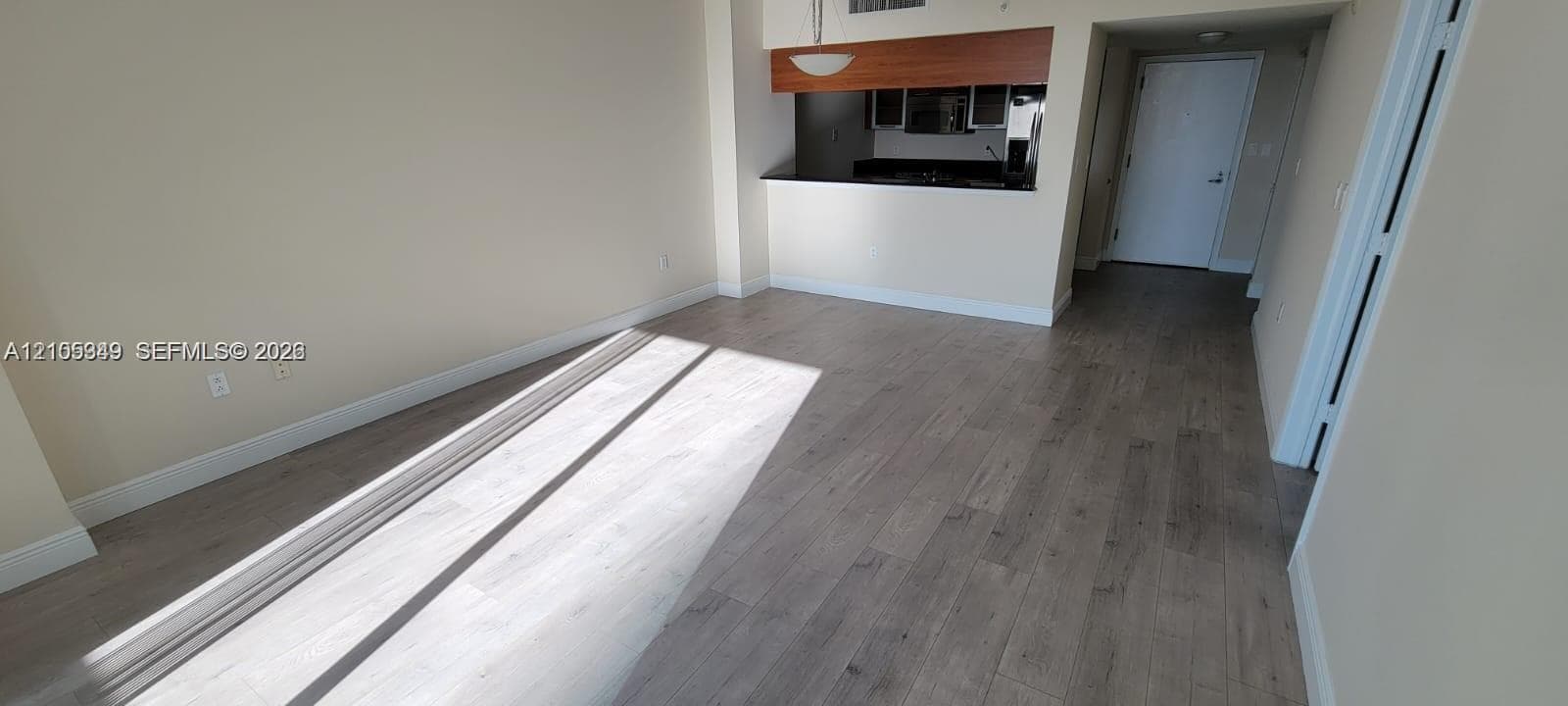 Wood-finish flooring, light-toned wall paint, and a pass-through kitchen opening with dark countertops