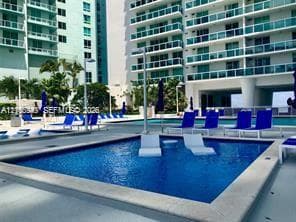 Outdoor pool area featuring a rectangular pool, concrete decking, and surrounding high-rise buildings with balconies