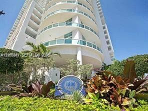 High-rise building with a curved facade, multiple balconies with glass railings, and a prominent address marker