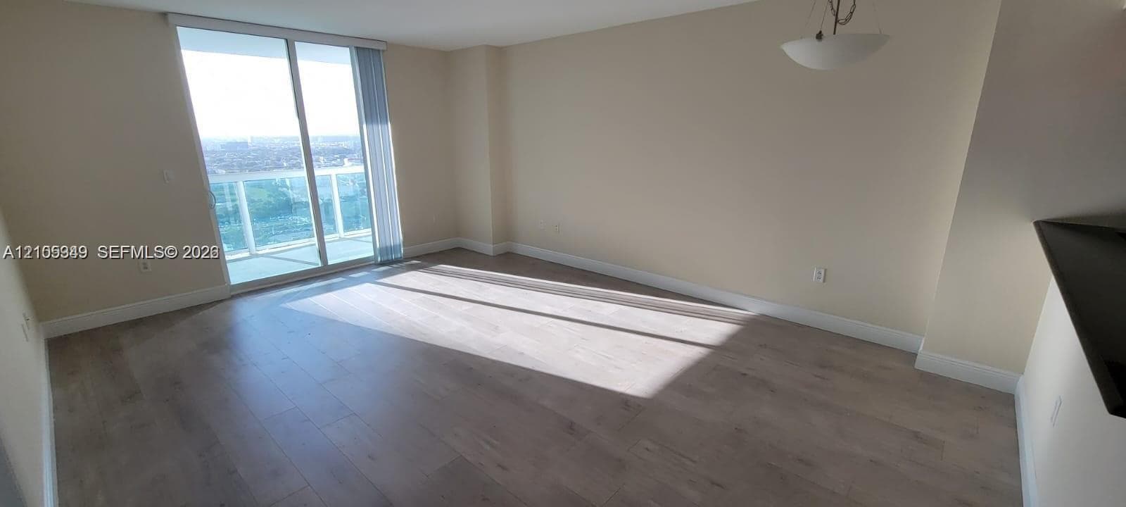 Spacious room featuring wood-finish flooring, light-toned walls, a glass sliding door, and an attached balcony with clear railings
