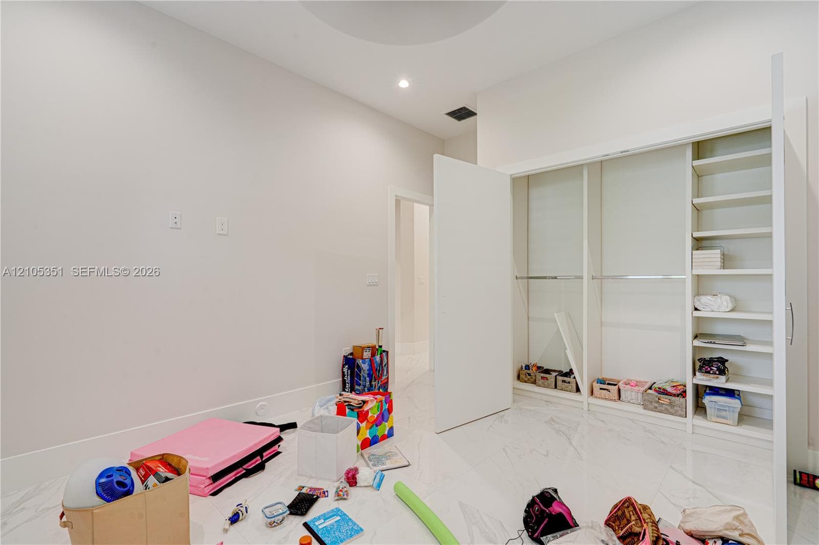 High-ceiling room with white stone-finish flooring and a built-in closet featuring integrated shelving and hanging rods