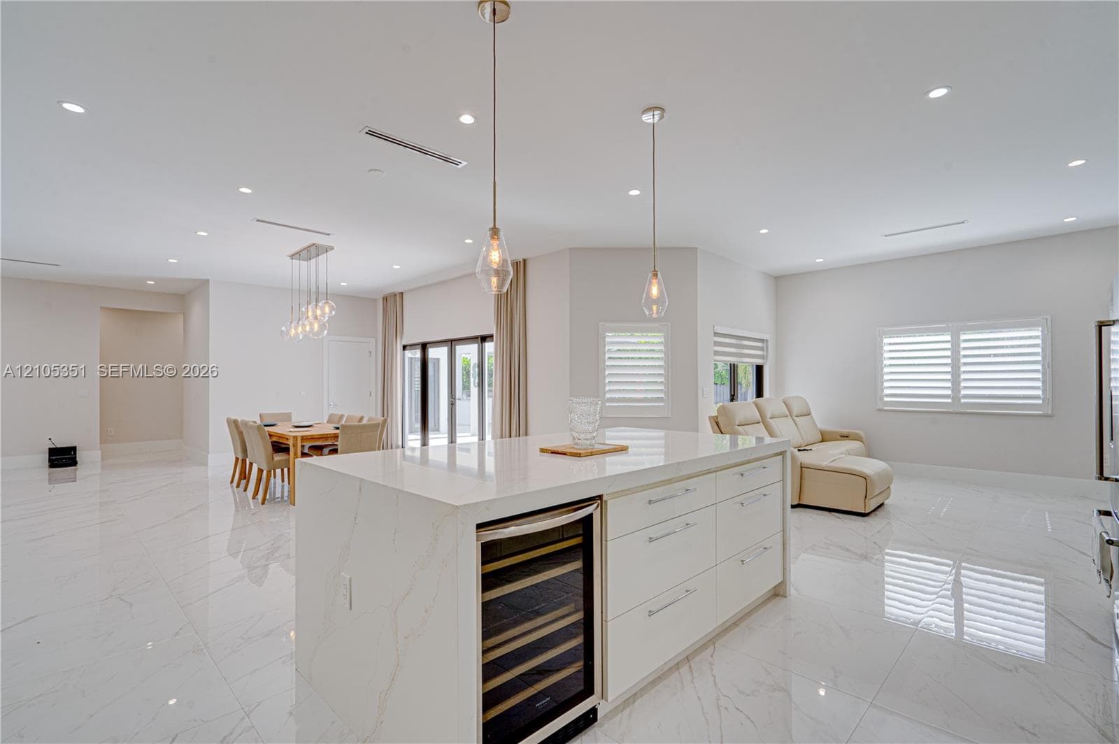 Kitchen featuring a central island with a stone-finish countertop and integrated beverage refrigerator, large-format tile flooring, recessed ceiling lighting, and multi-light pendant fixtures