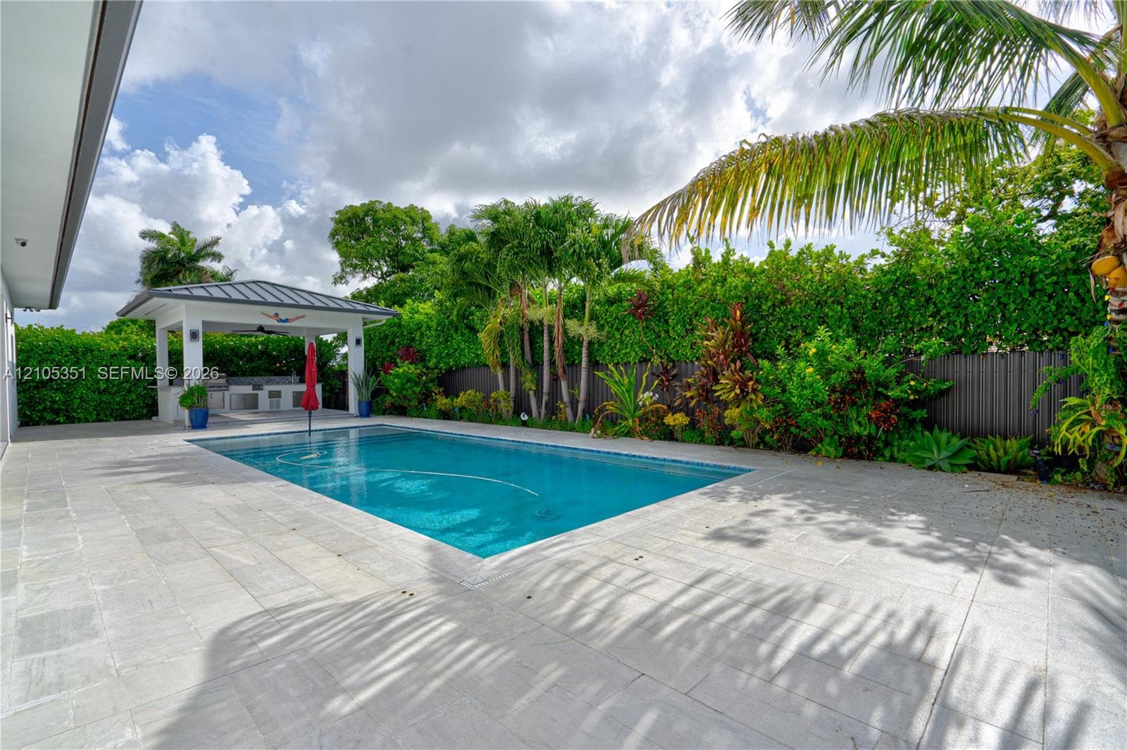 Backyard featuring an inground pool, stone-finish decking, and a covered outdoor kitchen structure