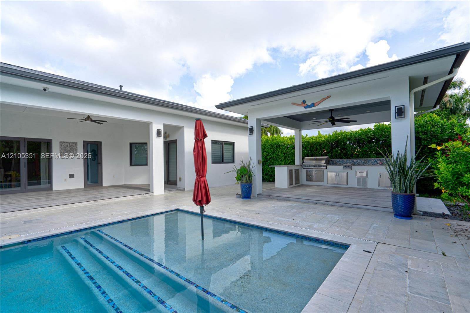 Outdoor living area featuring a custom swimming pool with step entry, covered patio, stone-finish decking, and built-in stainless steel kitchen grill