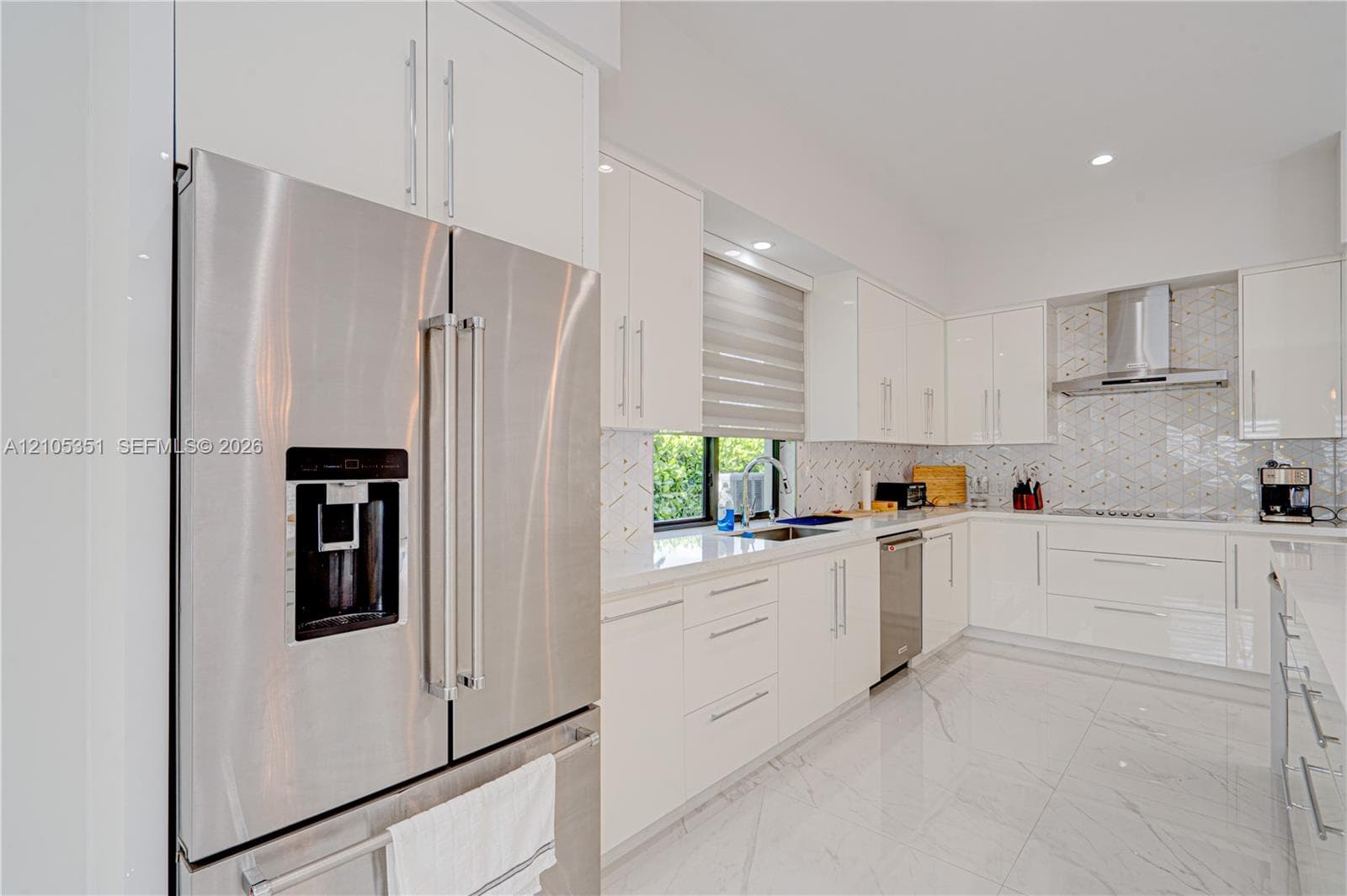 Kitchen featuring high-gloss white cabinetry, quartz countertops, stainless steel appliances, herringbone tile backsplash, and polished porcelain flooring