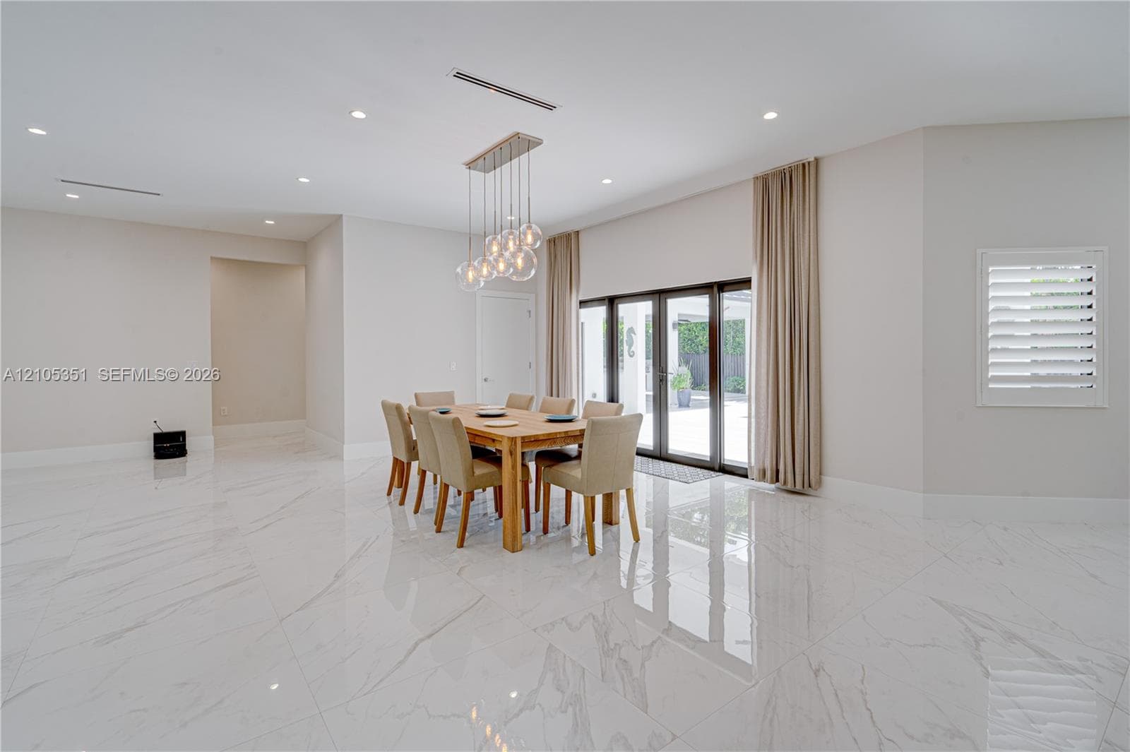 Large-format, polished stone flooring featuring distinct veining, multi-pendant glass orb chandelier, recessed ceiling lighting, and floor-to-ceiling multi-panel glass exterior doors