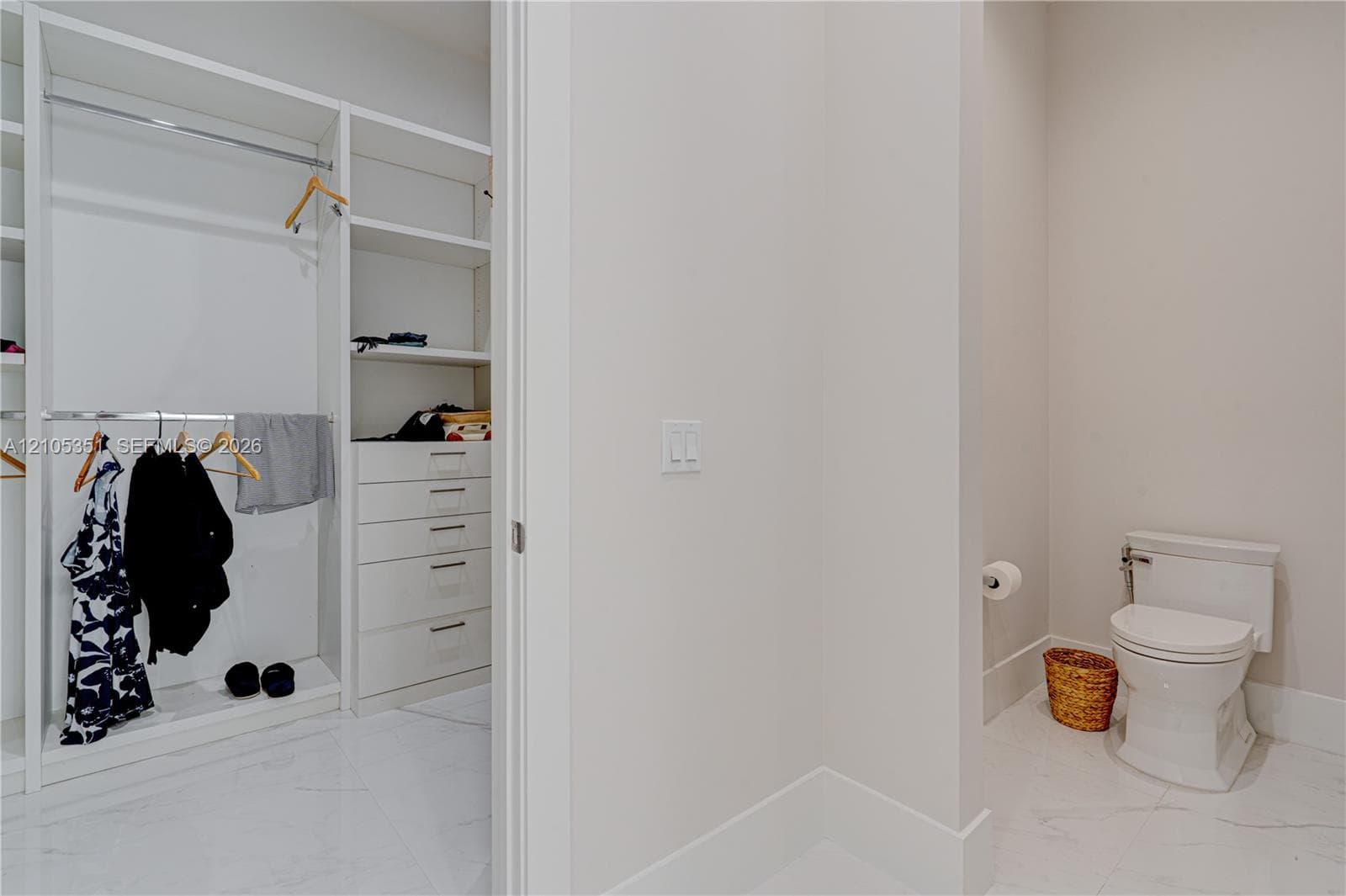 Custom walk-in closet featuring white built-in shelving and integrated drawer storage, paired with an enclosed water closet finished with stone-tile flooring