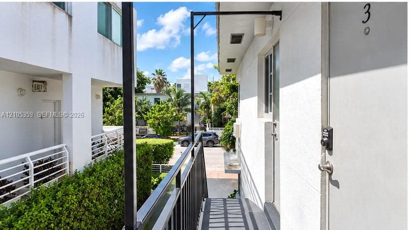 White stucco building exterior with a private entrance, exterior lighting fixture, and black metal railing