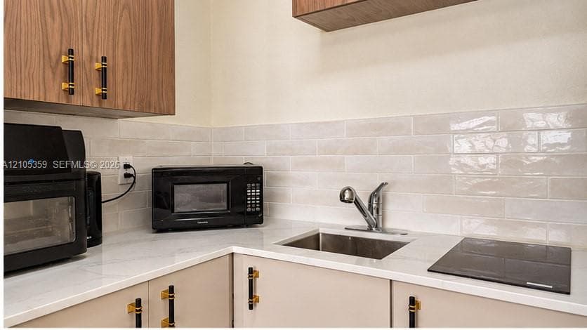 Wood-finish upper cabinetry, light-toned lower cabinetry, quartz-finish countertops, subway tile backsplash, and a stainless steel sink with a chrome faucet