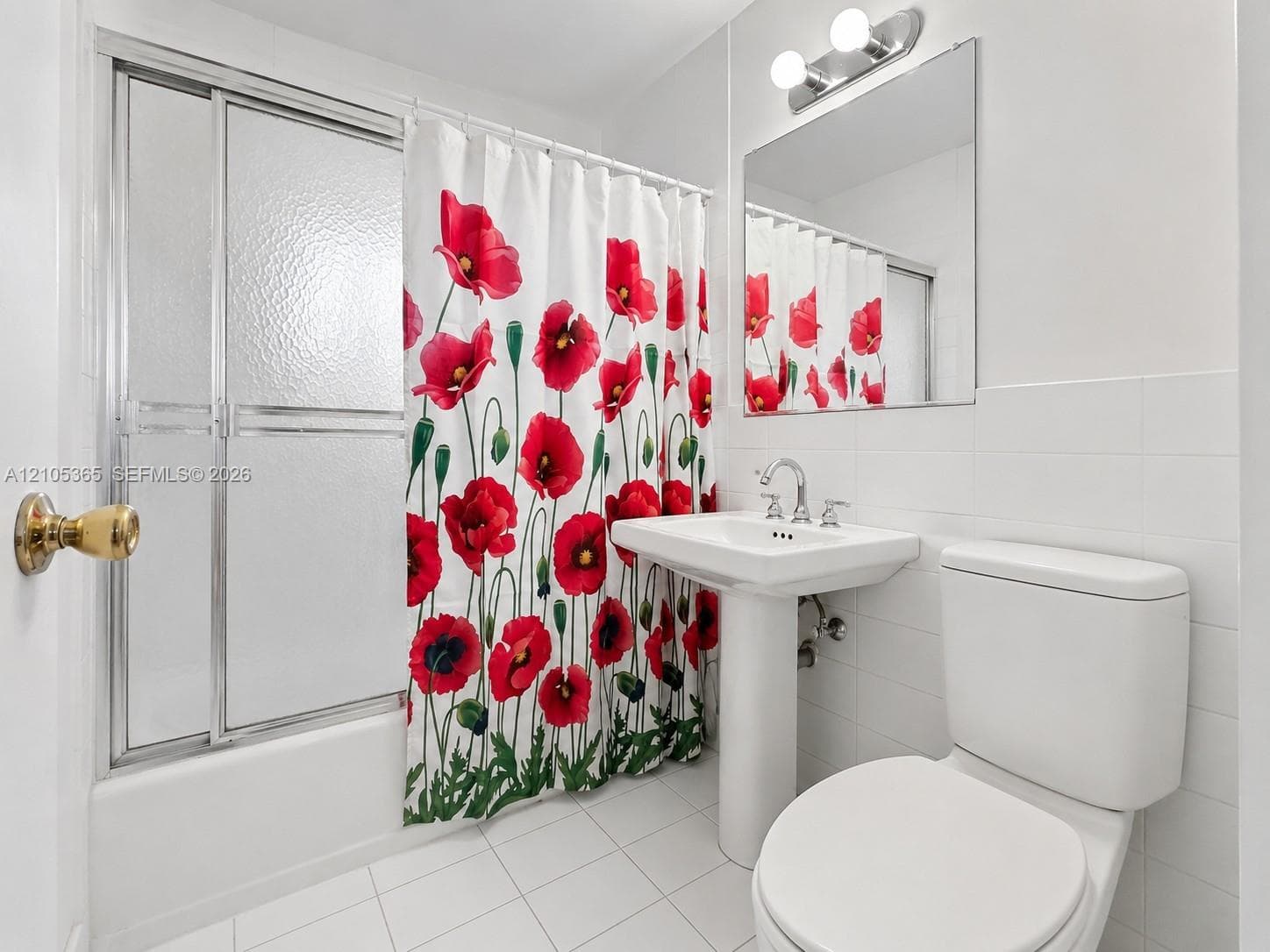 White tiled flooring, pedestal sink, wall-mounted mirror, and a tub with sliding glass doors