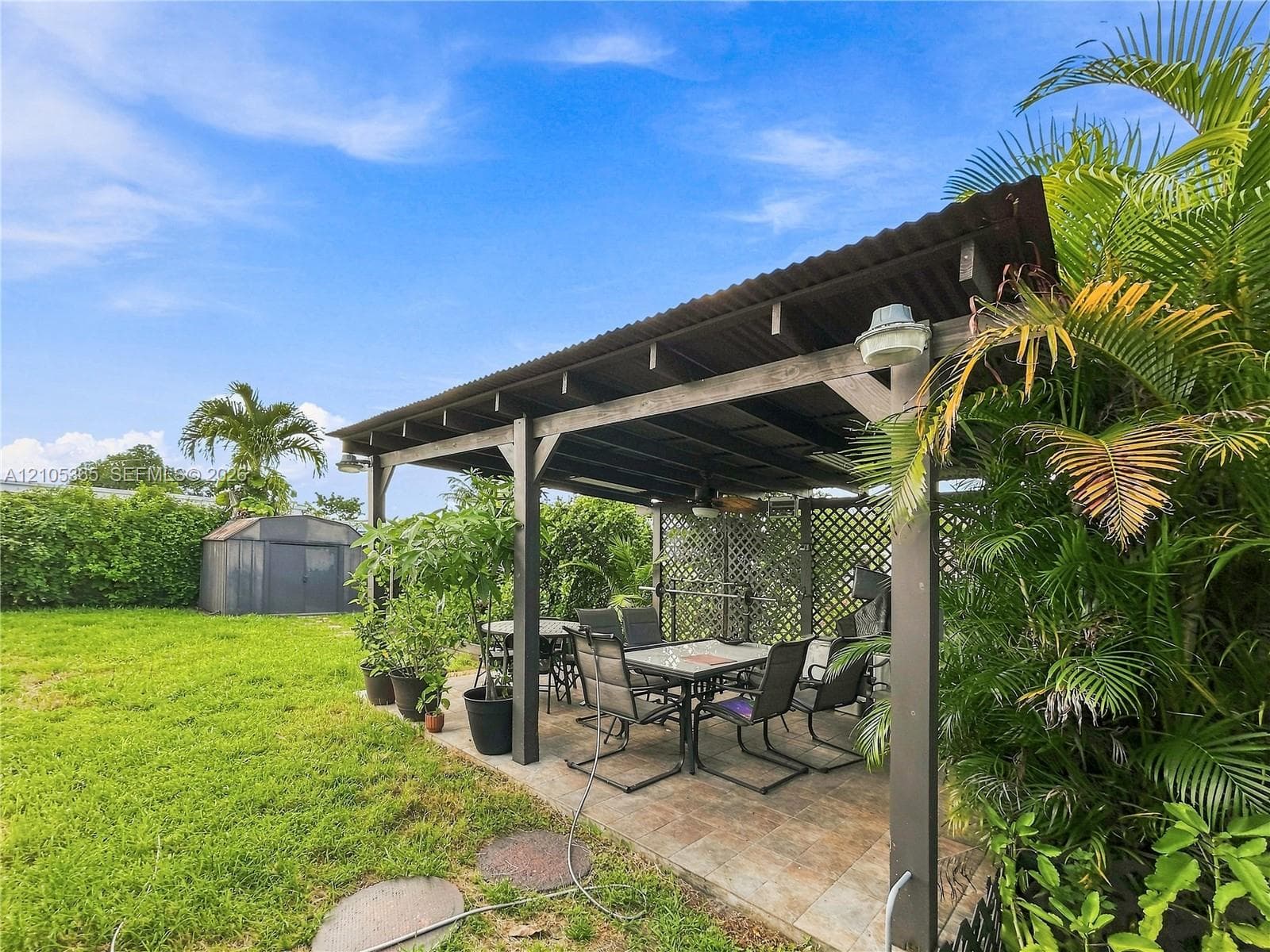 Expansive backyard featuring a covered patio with tiled flooring, a detached storage shed, and mature perimeter landscaping