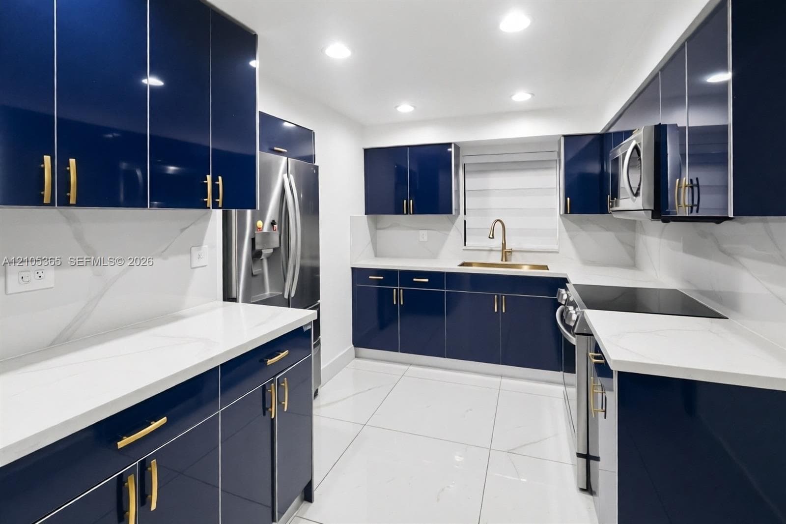 Contemporary kitchen featuring dark blue cabinetry with gold-tone hardware, white countertops, stainless steel appliances, and recessed lighting