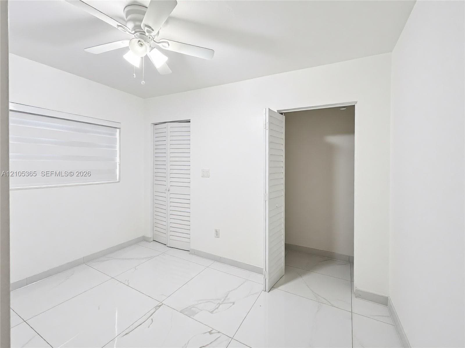 Recessed window with shade, ceiling fan, bi-fold louvered closet doors, and tile flooring
