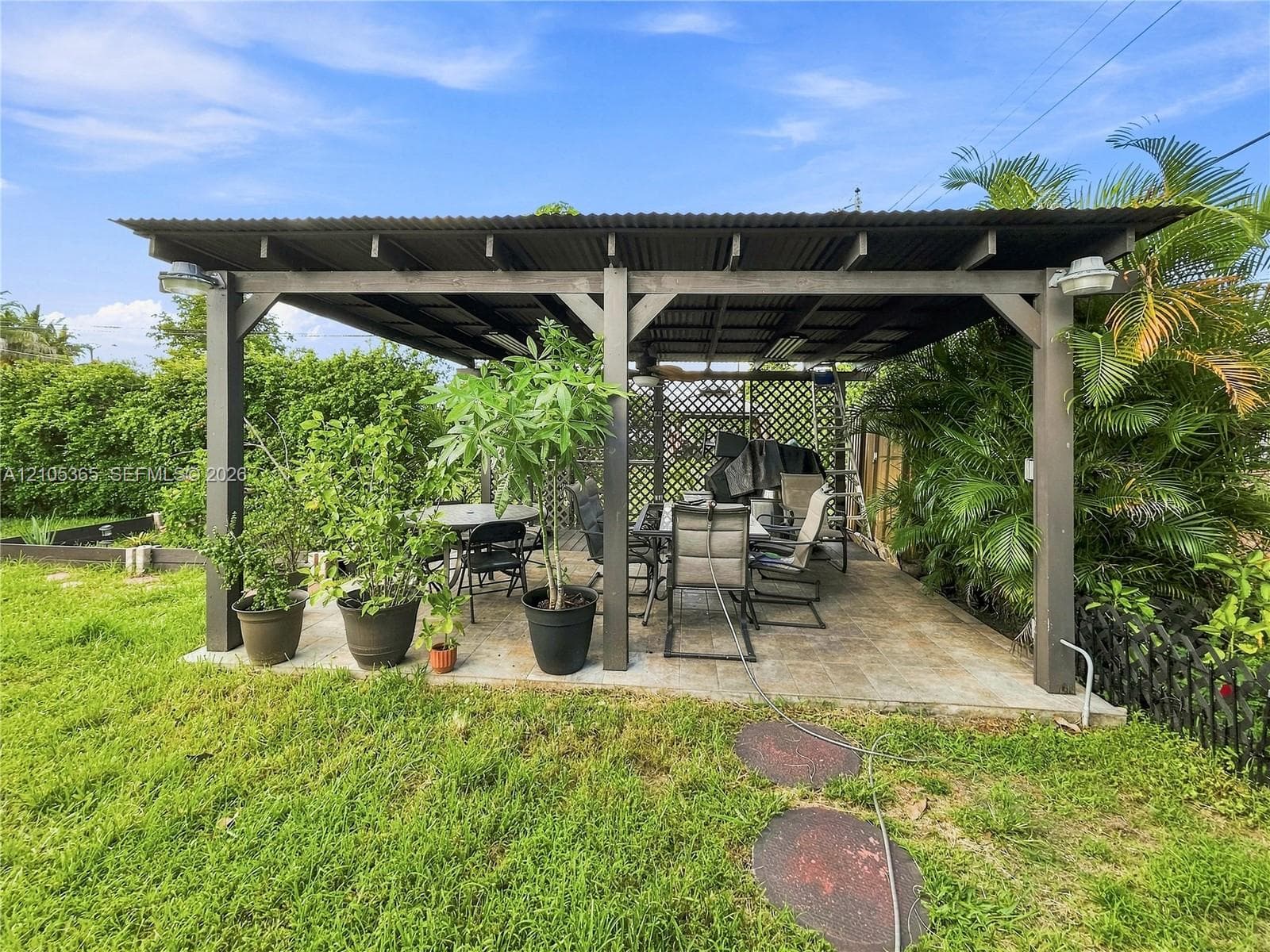 Expansive patio featuring a wood pergola with a corrugated roof, stone paver flooring, and perimeter lattice accents